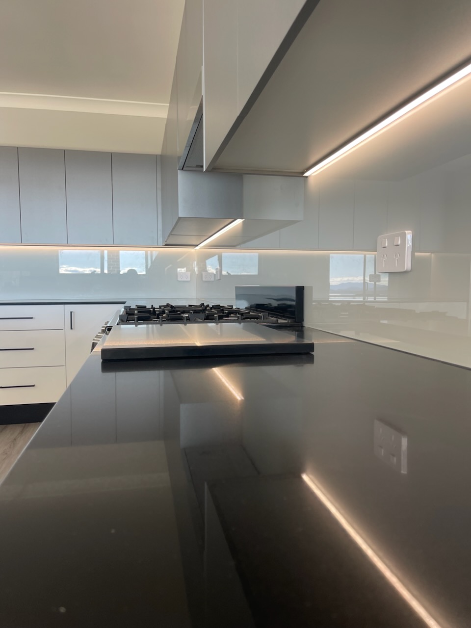 Kitchen with a continuous LED strip under the overhead cabinets reflecting off a glass splashback
