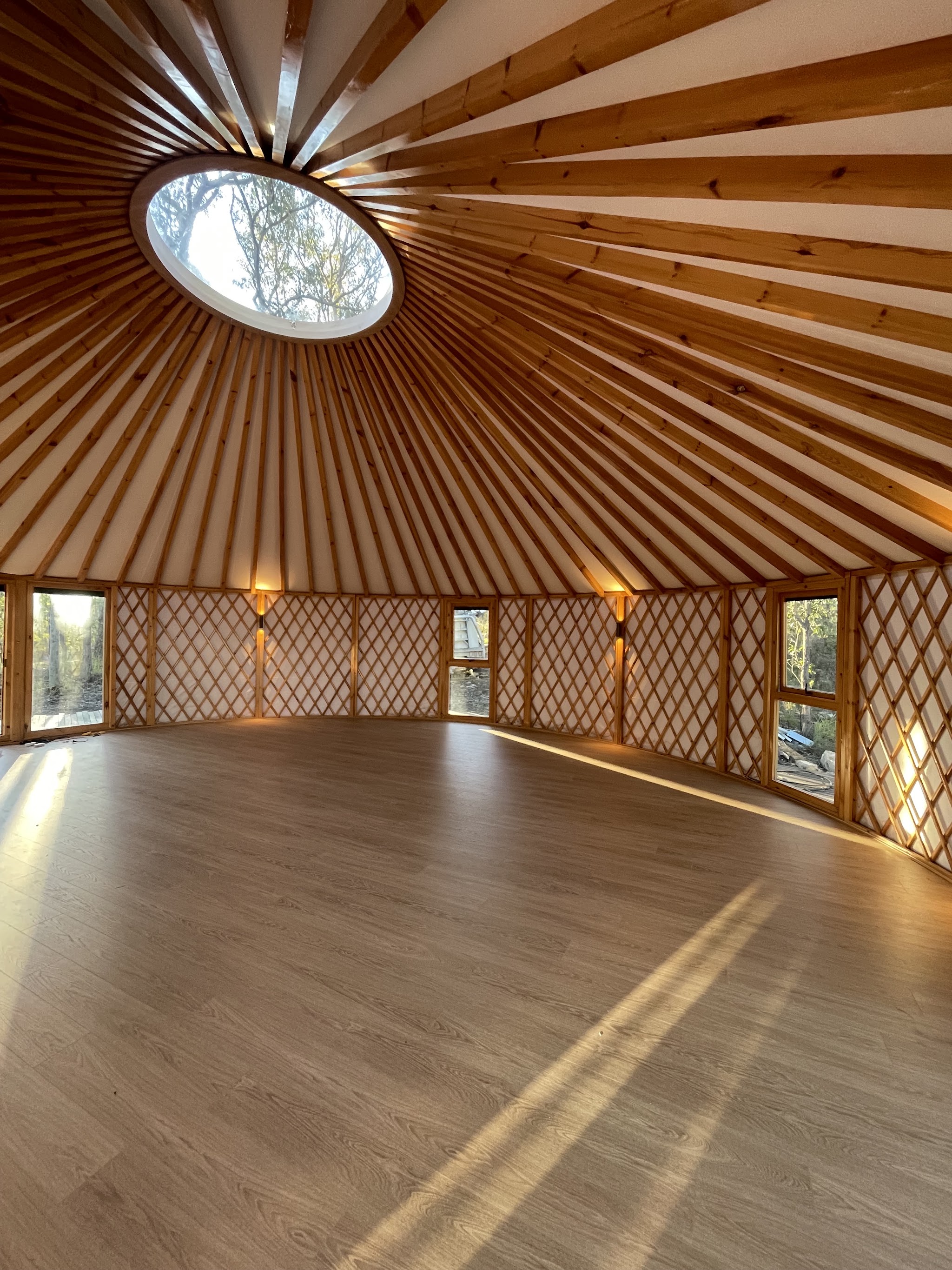Interior of a finished timber yurt with a circular skylight and warm uplights on the lattice walls